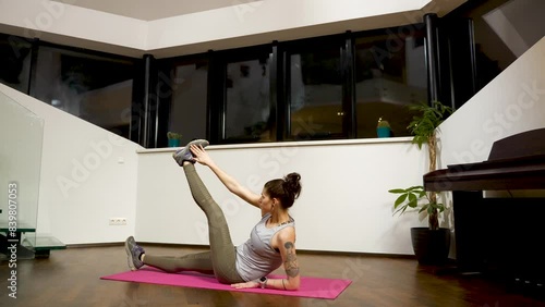 Lying on a pink yoga mat, a woman with tattoos is doing a reclined oblique twist exercise. photo