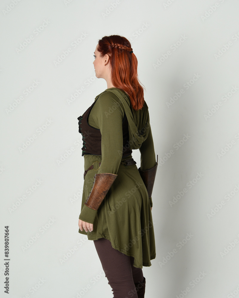 portrait of beautiful red haired female model, wearing green and brown medieval fantasy costume with tunic and armour. Standing pose facing away backwards , isolated on white studio background. portrait of beautiful red haired female model, wearing green and brown medieval fantasy costume with tunic and armour. Standing pose facing away backwards , isolated on white studio background.