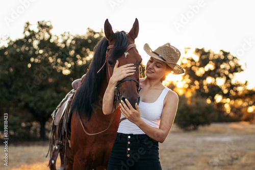 Young woman in hat walking with her horse in the countryside at sunset