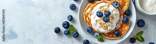 A stack of pancakes with blueberries and whipped cream on top. The pancakes are piled high and the blueberries are scattered all over the plate. Concept of indulgence and satisfaction photo