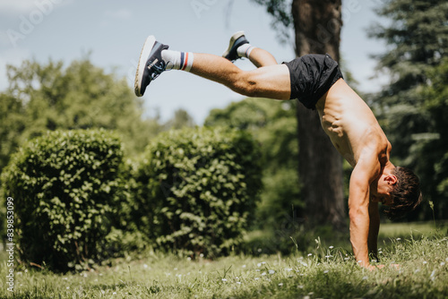 Athletic young man performing a handstand outdoors in a park on a sunny day, showcasing strength, fitness, and balance. photo