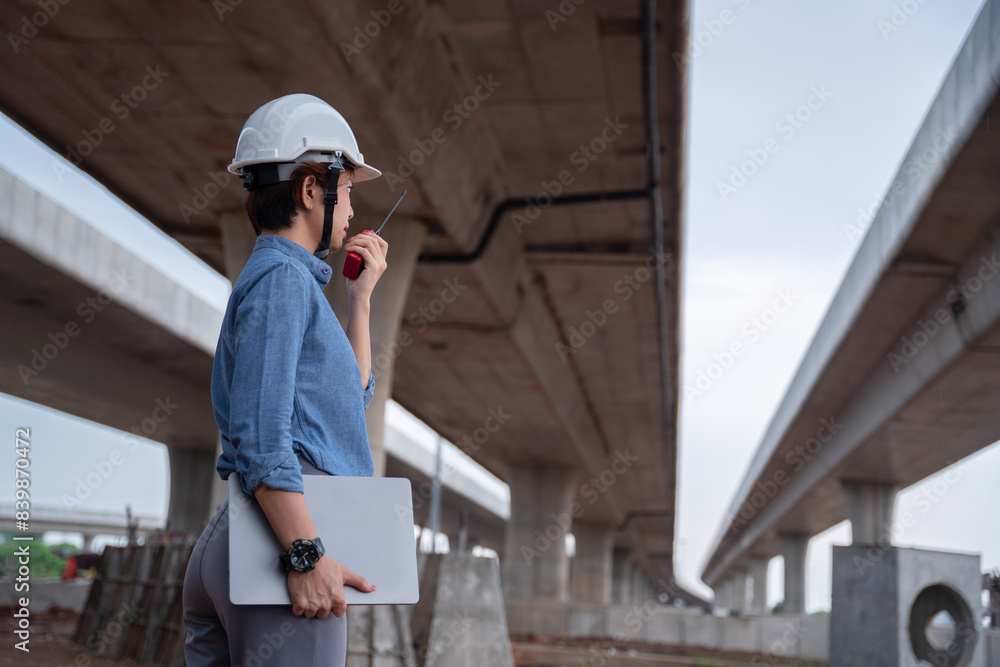 Asian female engineer with a laptop, managing the construction project under an overpass, ensuring safety and efficiency on-site. Asian female engineer with a laptop, managing the construction project under an overpass, ensuring safety and efficiency on-site.