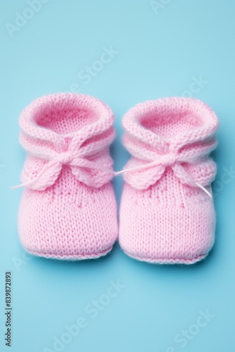 Two pink baby booties are knitted and placed on a blue background. Concept of warmth and comfort, as the booties are knitted and ready for a baby to wear