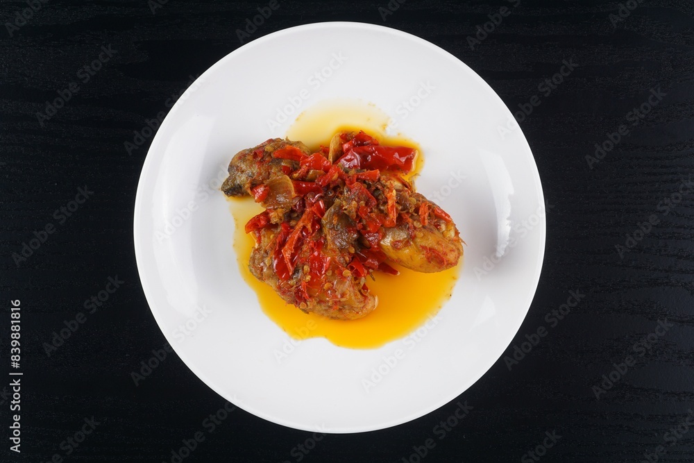 Indonesian typical balado fried chicken on a white plate on a black background with studio lighting Indonesian typical balado fried chicken on a white plate on a black background with studio lighting