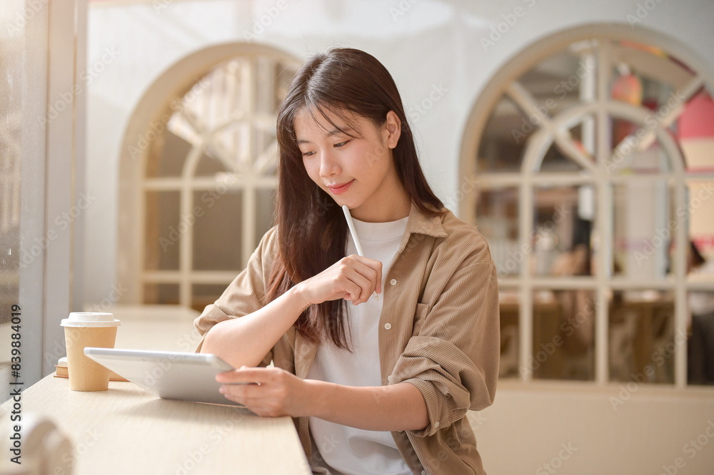 A young beautiful Asian woman in casual wear is sitting in a cafe and using her digital tablet. A young beautiful Asian woman in casual wear is sitting in a cafe and using her digital tablet.