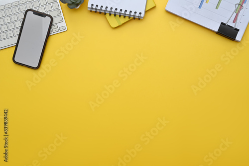 Smartphone, keyboard, notepad and financial documents on yellow background