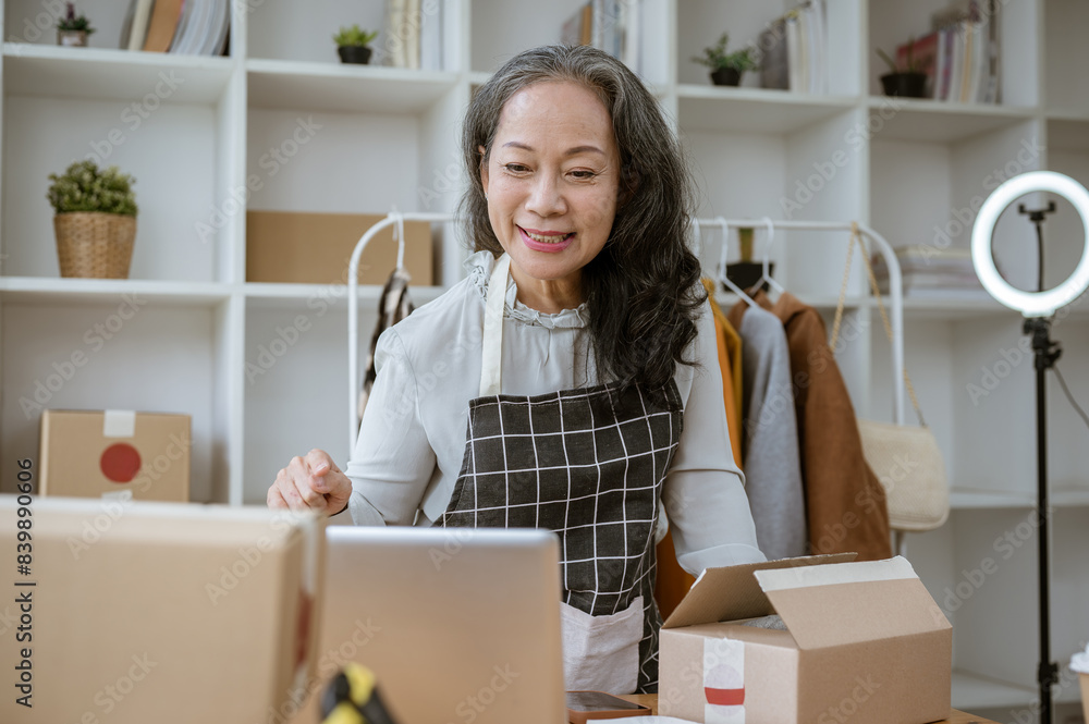 An attractive mature Asian female online clothes shop seller checking online orders on her computer. An attractive mature Asian female online clothes shop seller checking online orders on her computer.