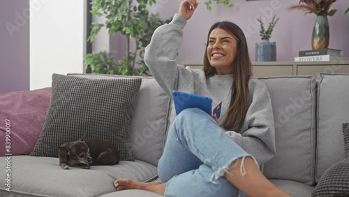 A smiling woman using a tablet and holding a credit card with a chihuahua beside her on a couch indoors photo