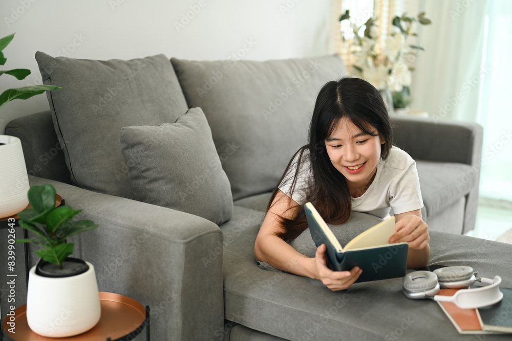Pretty young Asian woman reading book while lying on couch at home Pretty young Asian woman reading book while lying on couch at home