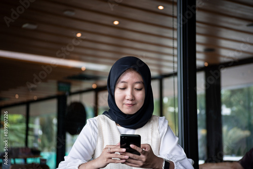 Valokuva indonesian hijab woman holding a cellphone in a coffee shop