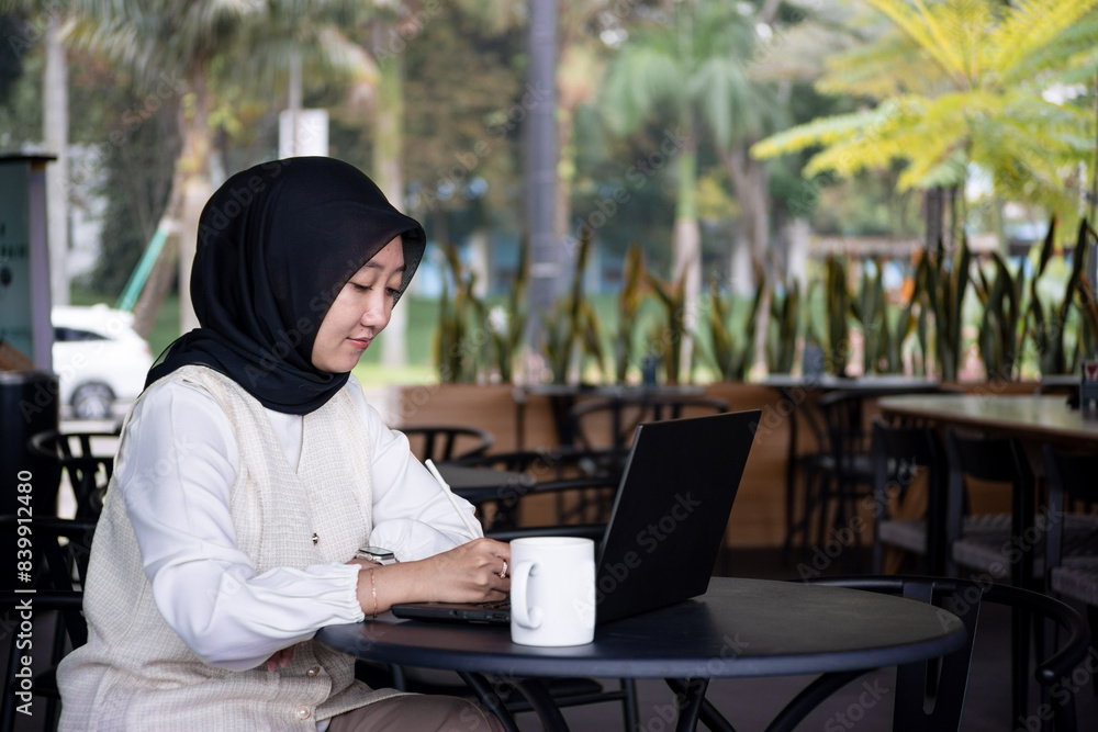 Beautiful young woman is working on a laptop and smiling, and thinking while sitting outdoors in a cafe enjoying a cup of coffee. Beautiful young woman is working on a laptop and smiling, and thinking while sitting outdoors in a cafe enjoying a cup of coffee.