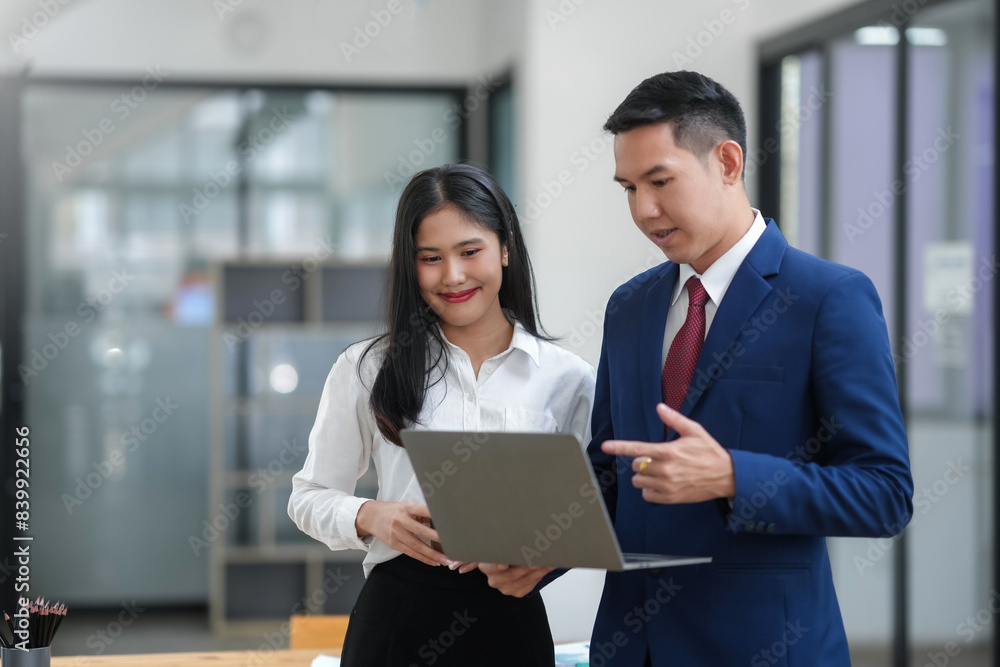 Professional colleagues discussing work on a laptop in a modern office setting. Business attire signifies a formal work environment. Professional colleagues discussing work on a laptop in a modern office setting. Business attire signifies a formal work environment.
