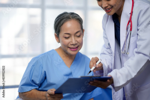 Two healthcare professionals reviewing documents, one holding a clipboard and the other pointing at it, in a medical setting.