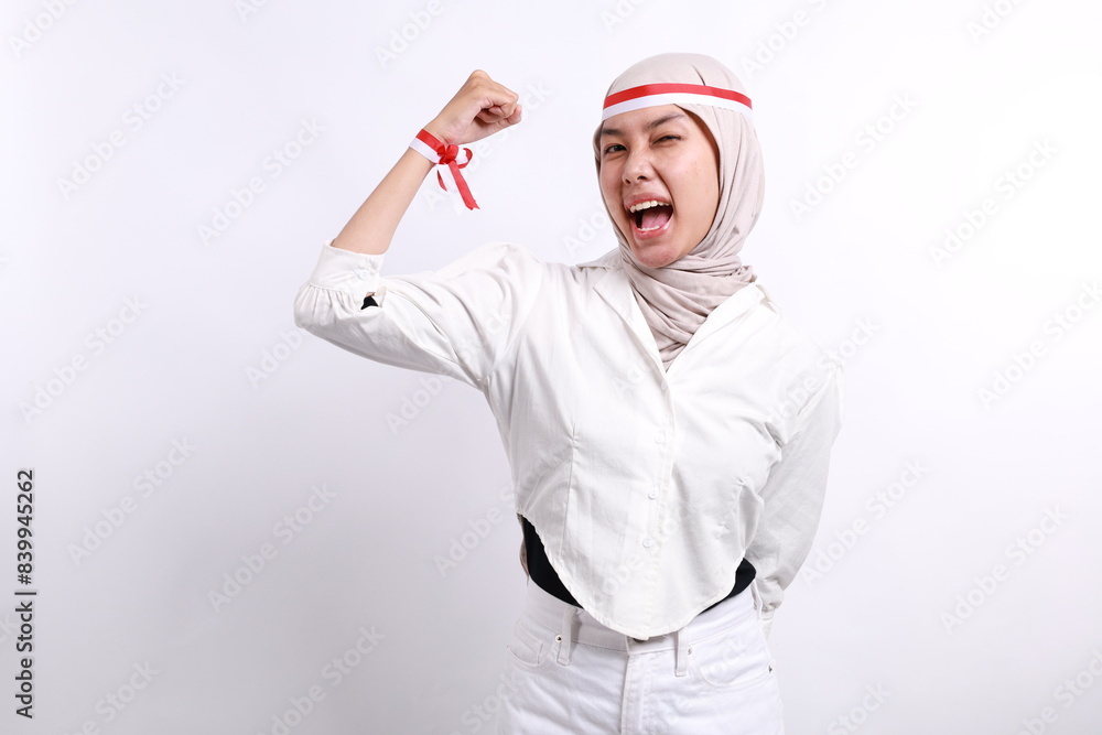 Overjoyed Young muslim woman wearing red white flag ribbon over white background glad to receive good news, clenching fist and making winning gesture. Indonesia's independence day concept. Overjoyed Young muslim woman wearing red white flag ribbon over white background glad to receive good news, clenching fist and making winning gesture. Indonesia's independence day concept.