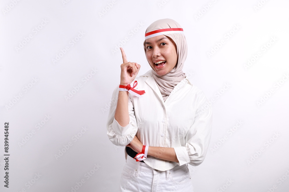 A happy Asian muslim woman wearing red white flag ribbon and pointing copy space on top of her, isolated by white background. Indonesia's independence day A happy Asian muslim woman wearing red white flag ribbon and pointing copy space on top of her, isolated by white background. Indonesia's independence day