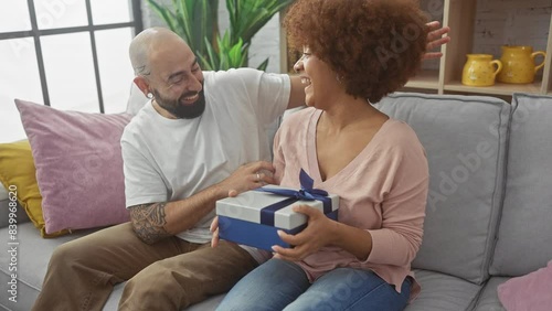 Interracial couple enjoying a happy moment indoors as man gives woman a gift box.