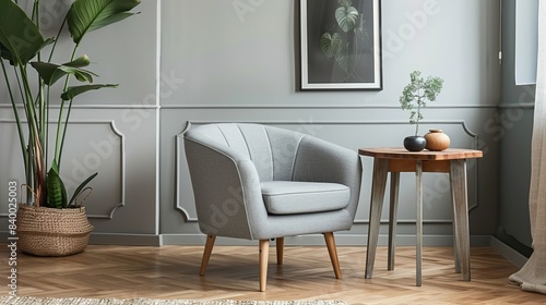 Grey armchair with plant and poster in the interior living room  next to wooden table