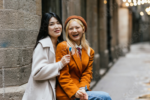 Photography Happy lesbian couple smiling while eating lollipops together outdoors