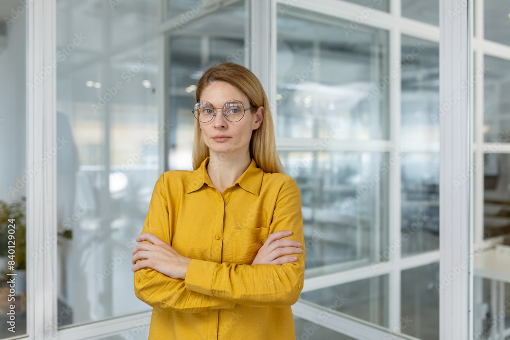 Confident businesswoman wearing a yellow shirt, standing with arms crossed in a modern office. Professional and determined female leader in a contemporary workplace. Confident businesswoman wearing a yellow shirt, standing with arms crossed in a modern office. Professional and determined female leader in a contemporary workplace.