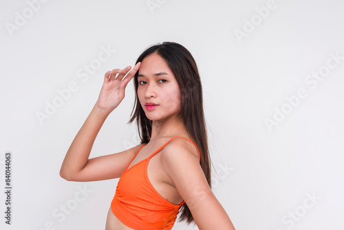 A young slim Asian woman wearing an orange bralette paired with a long skirt, striking a confident pose against an isolated white background. Perfect for fashion and lifestyle concepts. © Mdv Edwards