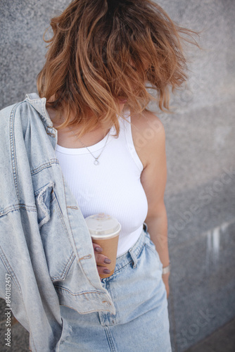 Plus size woman dressed jeans shirt, t-shert and skirt ealking in the street, Woman holding a cup of coffee.  The girl walking in windy day photo