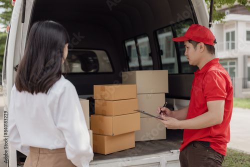 Young courier in red suit holds cardboard parcel box and woman transfers money with mobile to pick up parcel at home, online shopping and delivery of goods.