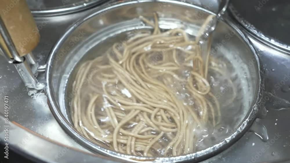 A person skillfully cools cooked soba noodles with ice cubes, preparing a refreshing Japanese dish. A person skillfully cools cooked soba noodles with ice cubes, preparing a refreshing Japanese dish.
