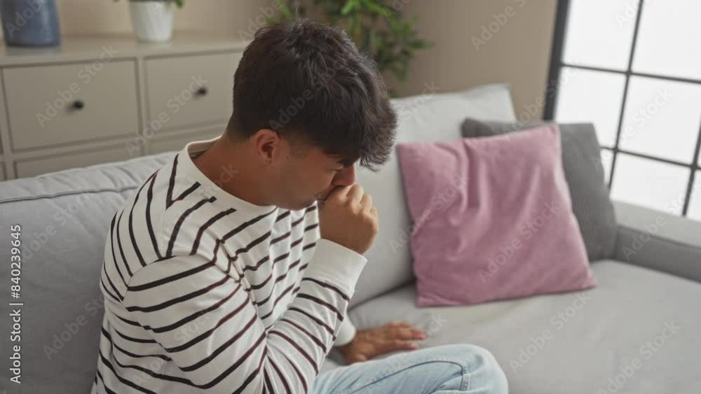 Young hispanic man coughing while sitting on a sofa in a cozy living room setting indoors, highlighting a moment of discomfort due to illness. Young hispanic man coughing while sitting on a sofa in a cozy living room setting indoors, highlighting a moment of discomfort due to illness.