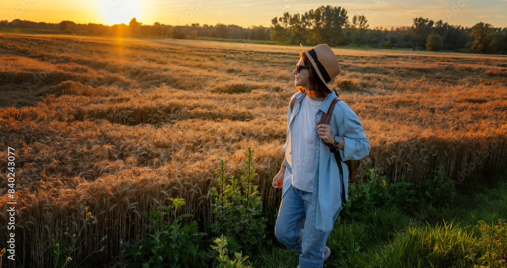 Young cheerful woman in a hat walking along a wheat field in the countryside in summer Young cheerful woman in a hat walking along a wheat field in the countryside in summer