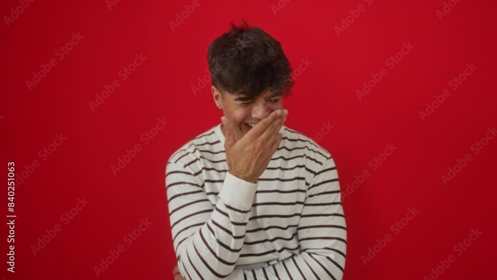 Laughing young hispanic man wearing stripes t-shirt, covering mouth with hand, embarrassed and giggling, isolated over red background, gossip and cheerful joy Laughing young hispanic man wearing stripes t-shirt, covering mouth with hand, embarrassed and giggling, isolated over red background, gossip and cheerful joy