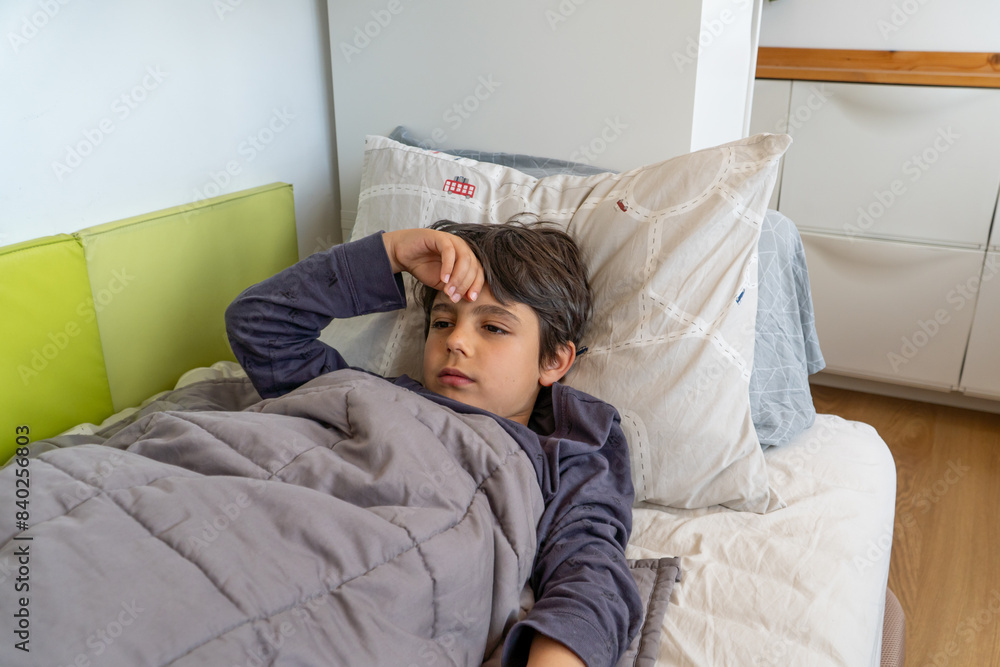 Boy feeling unwell lying in bed holding his head Boy feeling unwell lying in bed holding his head
