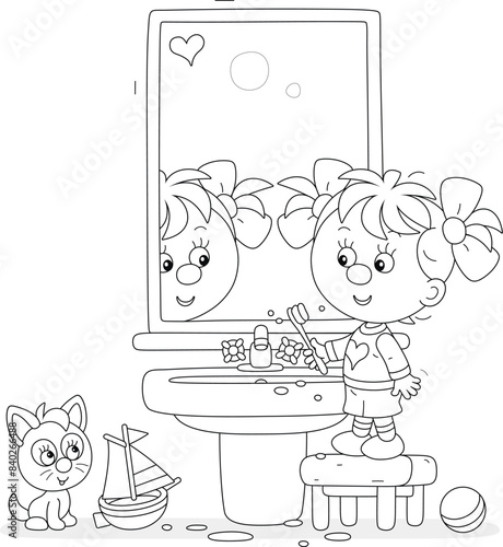 Funny little girl brushing her teeth at a mirror and washbasin in a bathroom with toys, black and white vector cartoon illustration for a coloring book