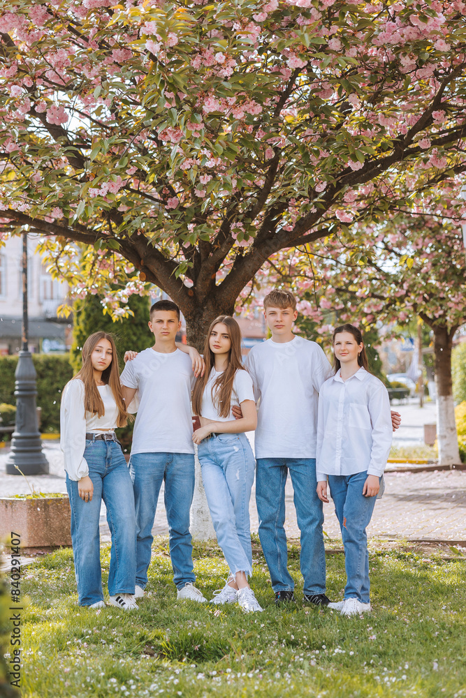 Obraz premium A group of five people are posing for a picture in front of a tree. Scene is lighthearted and fun, as the group is smiling and enjoying each other's company. The setting of the image