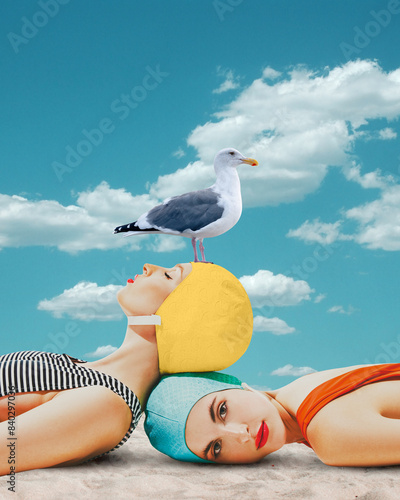 Obraz na plátně Beautiful young girls in swimming cap and swimsuits lying on beach with seagull against blue sky background