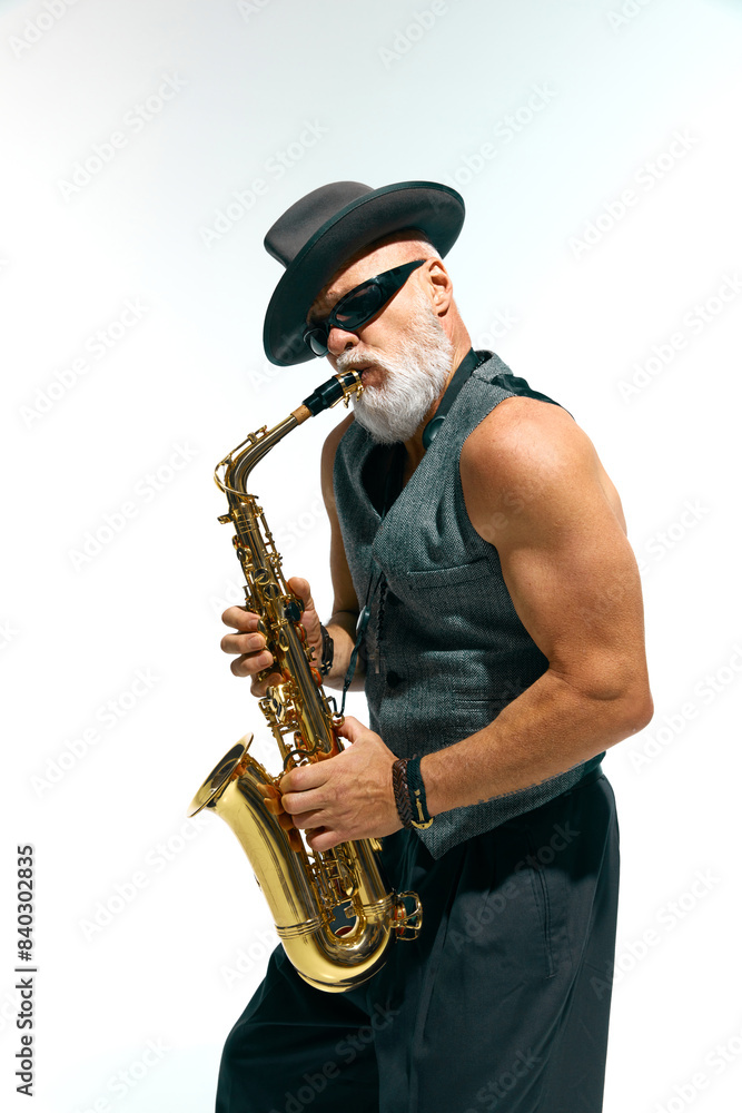 Naklejka premium Artistic mature man with beard dressed vintage fashion outfit plays golden saxophone against white studio background. Concept of music, festivals, contemporary art, hobby, creativity. Ad