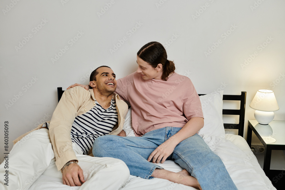 A young gay couple in casual attire shares a laugh and a comfortable moment together on a bed in a modern apartment. A young gay couple in casual attire shares a laugh and a comfortable moment together on a bed in a modern apartment.