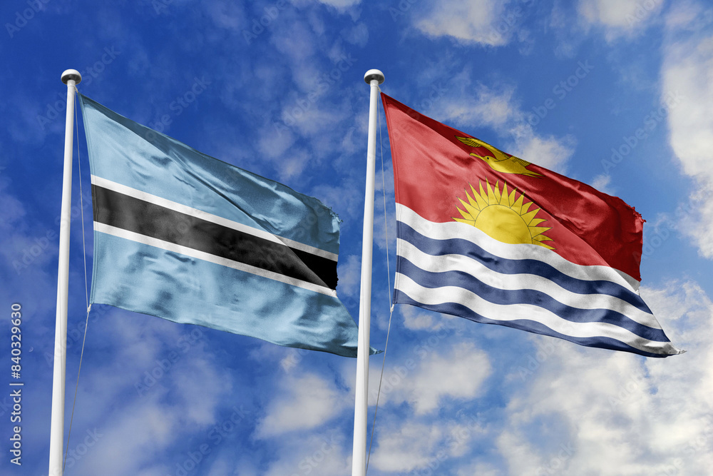 Fototapeta premium 3D illustration. Botswana and Kiribati flags waving in the sky. High detailed waving flag. 3D render. Flags fluttered in the cloudy sky, symbolizing diplomatic relations.