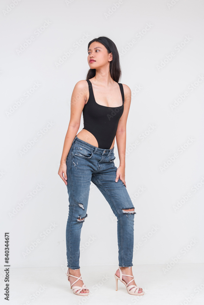 Front view of a fierce looking young asian woman of ideal height and figure in a black bodysuit and ripped jeans Isolated on a white background. Looking to her side. Whole body photo. Front view of a fierce looking young asian woman of ideal height and figure in a black bodysuit and ripped jeans Isolated on a white background. Looking to her side. Whole body photo.