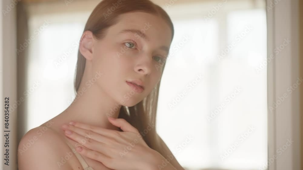 Slow motion. Pretty young slim blonde girl and bare shoulders touches her neck with her fingers and turns her body in front of a mirror. Woman applying body lotion and massaging neck skin. Body care Slow motion. Pretty young slim blonde girl and bare shoulders touches her neck with her fingers and turns her body in front of a mirror. Woman applying body lotion and massaging neck skin. Body care