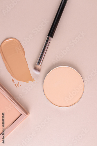 A stroke of foundation, a round block of compact powder, a makeup brush on a beige background. The top vertical view. The concept of beauty, makeup.