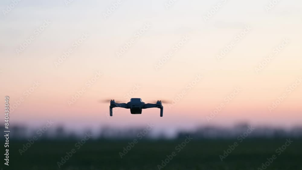 Silhouette of small commercial drone flying in the evening. Quadcopter in flight, small drone shooting photos, filming video
