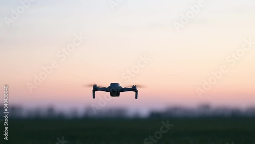 Silhouette of small commercial drone flying in the evening. Quadcopter in flight, small drone shooting photos, filming video