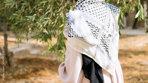 Pregnant female wearing palestine keffiyeh  in olive tree field holding branch of olive tree in her hand while touch her tummy in the other hand praying for her child peace and safe future 