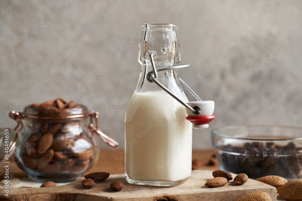 A bottle of vegan almond milk on a wooden table, with almonds and raisins in the background A bottle of vegan almond milk on a wooden table, with almonds and raisins in the background