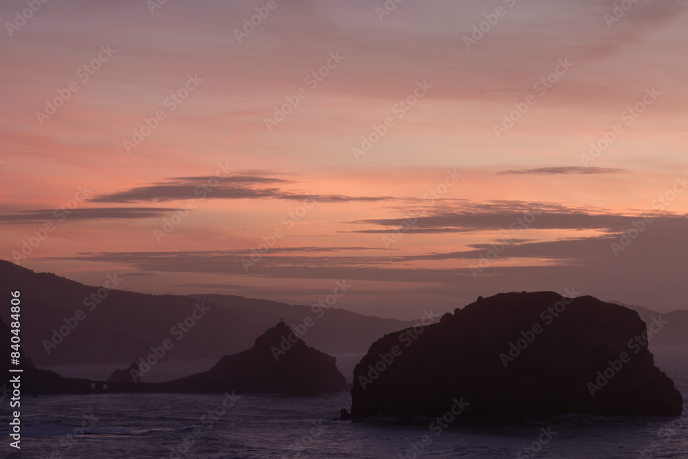 A serene sunset with silhouetted mountains and rock formations against a gradient sky, evoking peace and tranquility in san juan de gaztelugatxe A serene sunset with silhouetted mountains and rock formations against a gradient sky, evoking peace and tranquility in san juan de gaztelugatxe