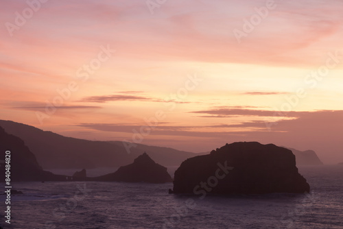 A serene sunset over the ocean  with silhouetted rocky islands and warm hues of pink and orange in the sky