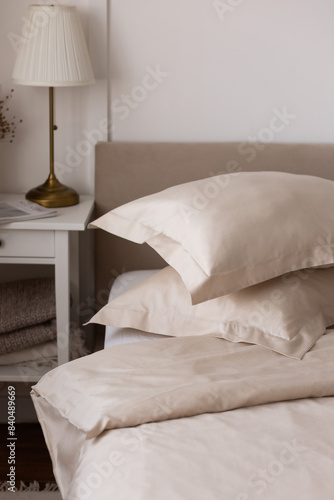 a stack of beige satin bed linen (satin, lyocell, silk): duvet cover and pillowcases with borders in a cozy interior. Cozy home concept. Home textiles