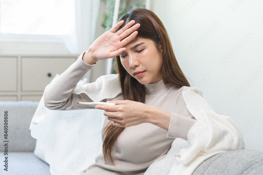 Sick, influenza asian young woman, girl headache have fever, hand touching forehead, holding thermometer for check measure body temperature, illness while sitting rest on sofa at home. Health care. Sick, influenza asian young woman, girl headache have fever, hand touching forehead, holding thermometer for check measure body temperature, illness while sitting rest on sofa at home. Health care.