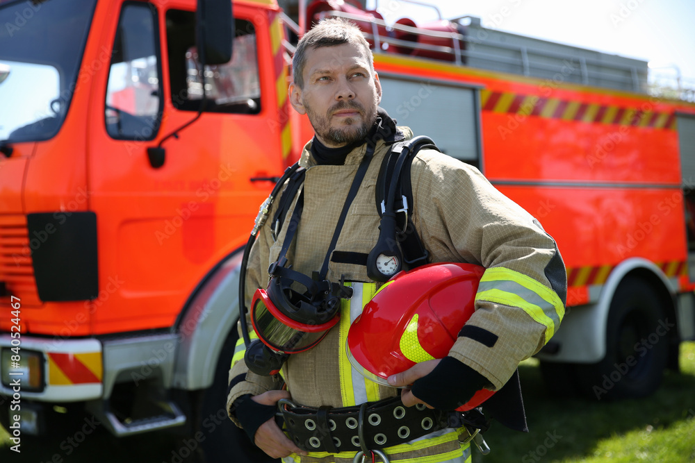 Firefighter in uniform with helmet near fire truck outdoors Firefighter in uniform with helmet near fire truck outdoors