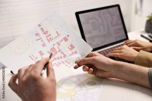 Cartographers working with cadastral maps at white table in office, closeup
